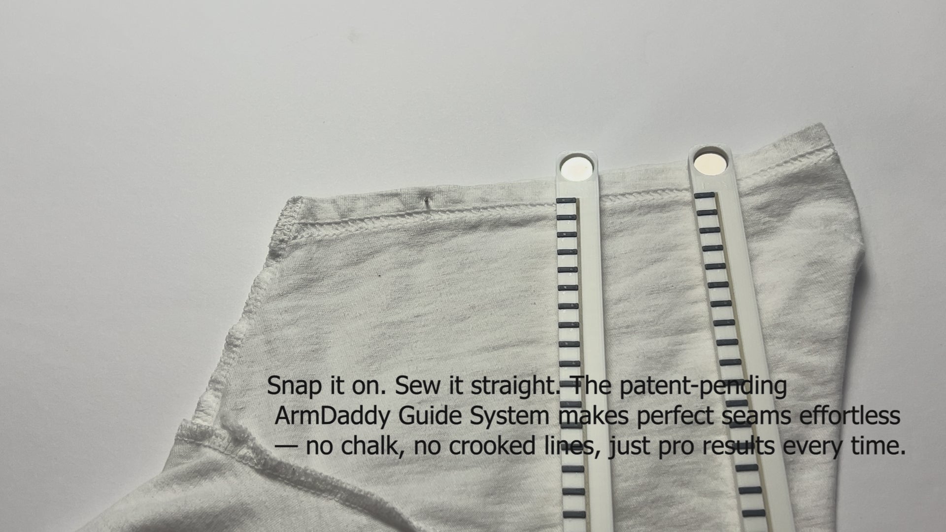 Video shows an individual using the ArmDaddy Thread Aid and Guide System. The user snaps the guide onto the T-shirt sleeve and the text on the screen says “Snap it on. Sew it straight. The patent-pending ArmDaddy Guide System makes perfect seams effortless --- no chalk, no crooked lines, just pro results every time.” The video then shows the user demonstrating the ArmDaddy Thread Aid. He threads a needle and ties a knot using the Thread Aid. The text on the video says “Thread it. Knot it. Done in 30 seconds